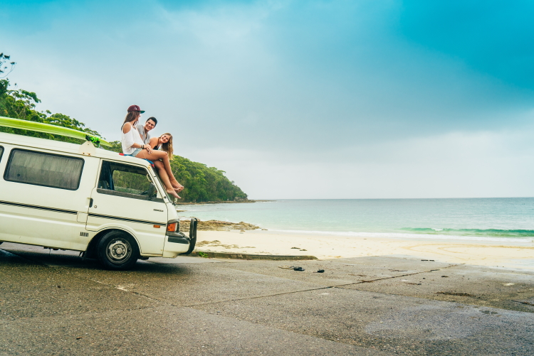 Drei Personen sitzen während ihrer Work and Travel Zeit in Australien auf ihrem Campervan am Strand.